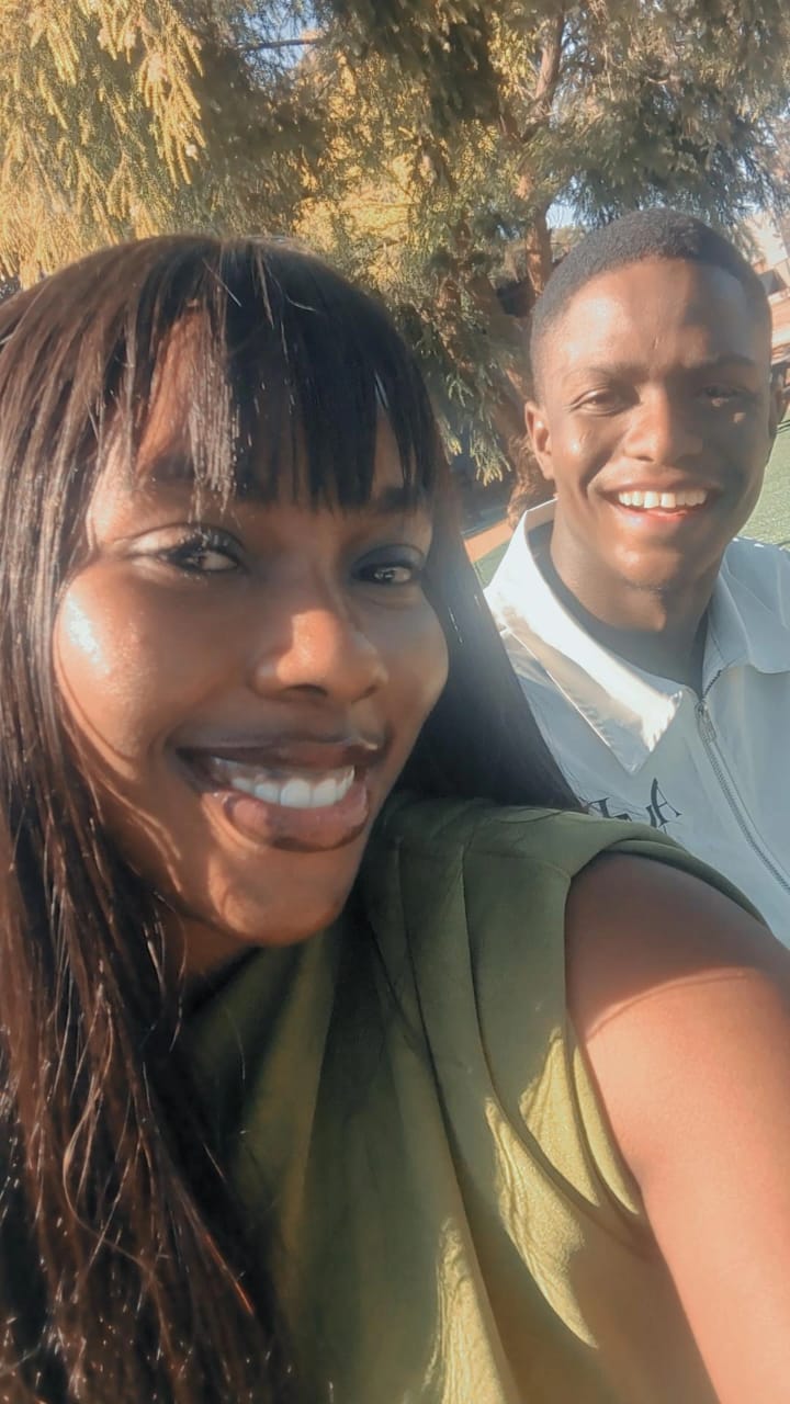 Natalie smiling in the sunlight beside a friend under a tree
